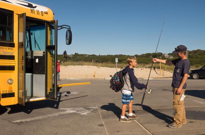 Off the school bus, ready to fish: Marshall Carroll hands Brooks Carroll his fishing rod.