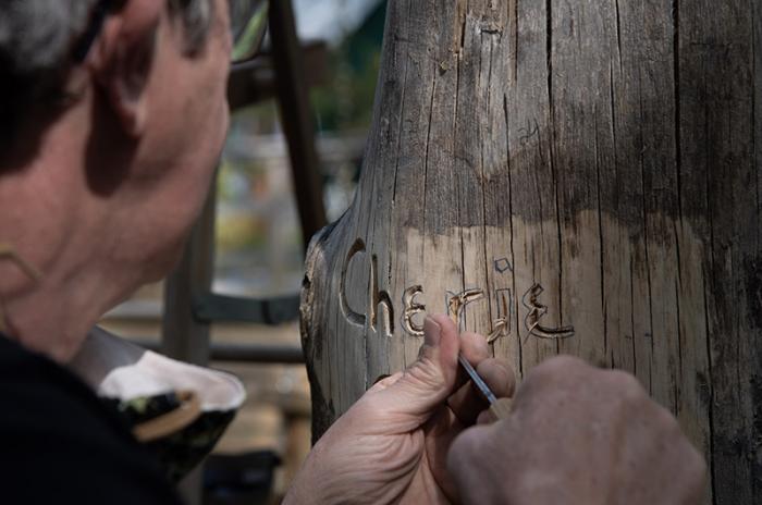 More than two dozen names are being carved into repurposed tree trunks that support the camp’s hilltop swing pergola.