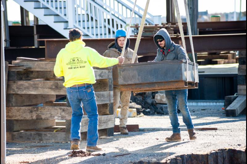Workers help crane lower heavy materials.